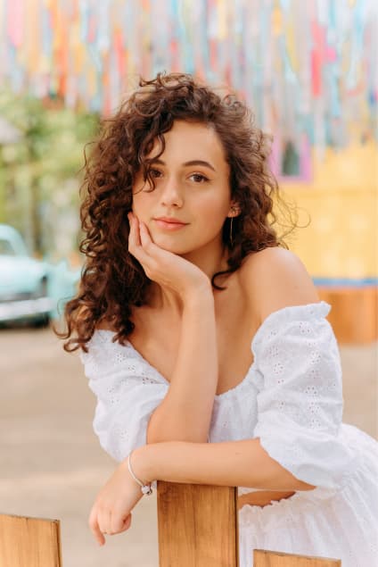 Imagem de uma mulher com o cabelo cacheado e roupa branca servindo apenas para a ilustração da página inicial